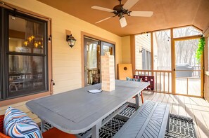 Une terrasse couverte avec une table et des chaises, un ventilateur de plafond et une vue sur l’extérieur.