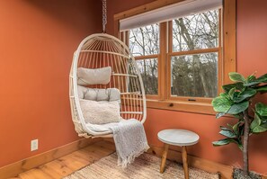 Una habitación con una silla colgante, una mesita y una planta en maceta.