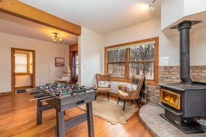 A cozy room with a foosball table, a fireplace, and a large window with a view of trees.