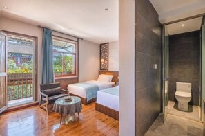 A hotel room with two beds, a small round table, a sofa, a balcony with a view of traditional architecture, and a modern bathroom with a glass shower enclosure. - Guilin Inn Jianshui (Jianshui)