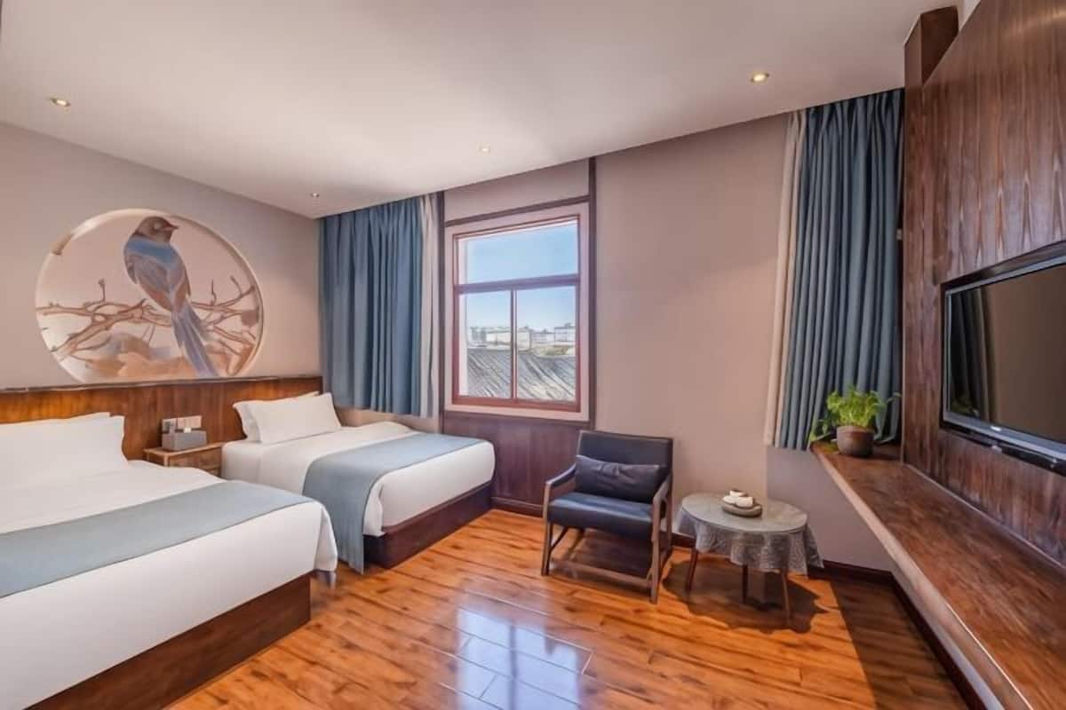 A hotel room with two beds, a TV, a small table, and a window with curtains.
