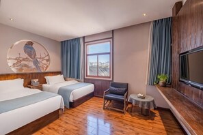 A hotel room with two beds, a TV, a small table, and a window with curtains.