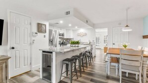 Una cocina moderna con una isla central, taburetes de bar y una mesa de comedor con sillas.