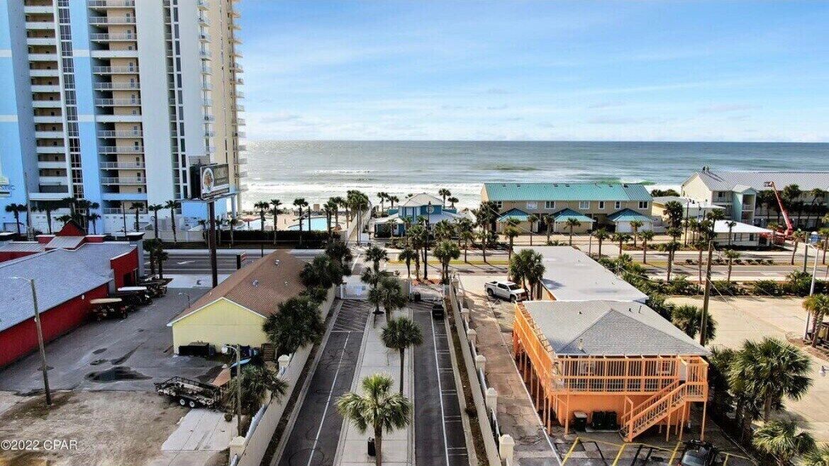 A coastal hotel with a parking lot, beach view, and a large building in the background.