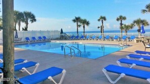 Un área de piscina con sillas reclinables azules y palmeras.