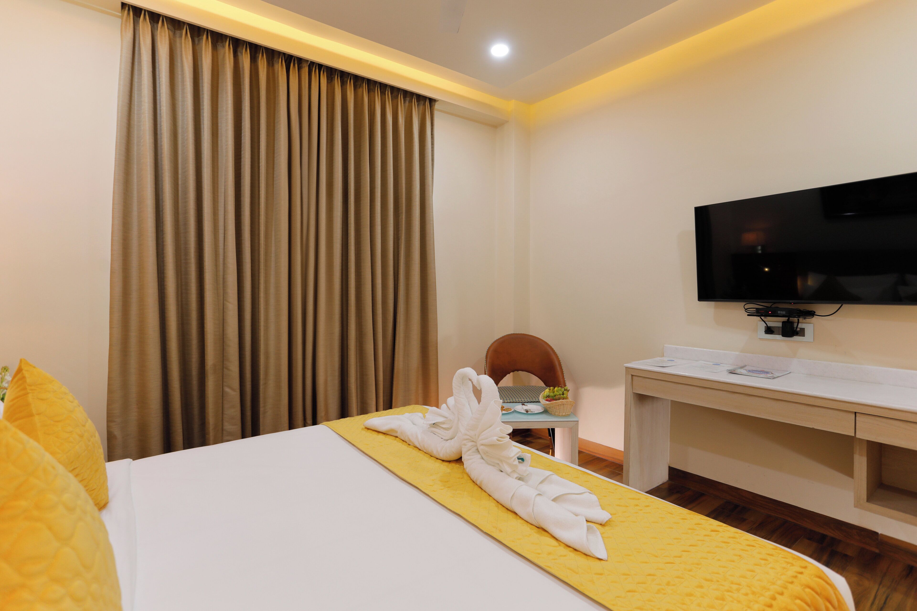 A hotel room with a bed, a desk, a television, and a window with curtains.