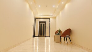 A hallway with a shiny floor, an elevator, and two chairs with a small table and flowers. - HOTEL DOLPHIN GRAND  (Varanasi)