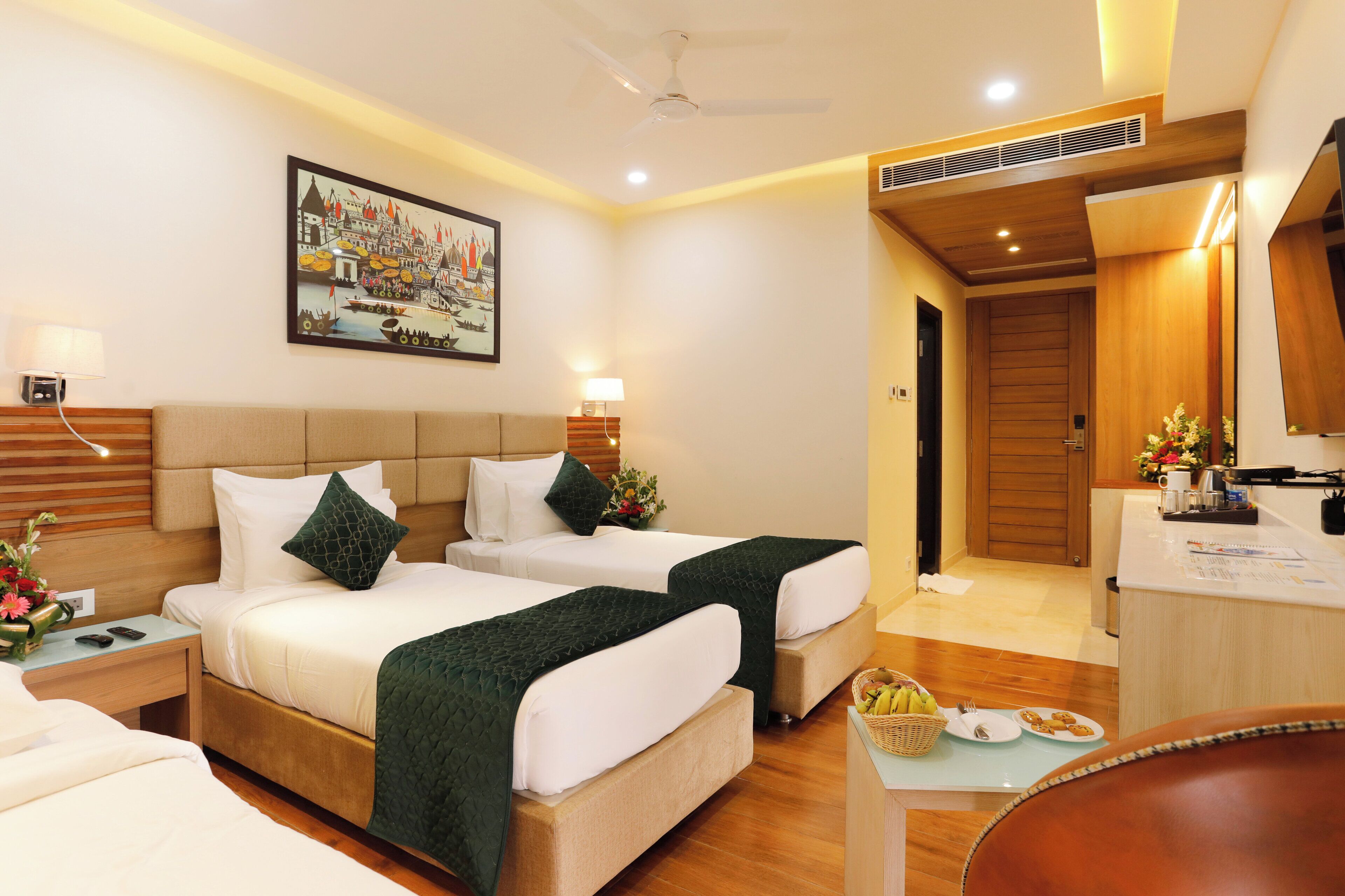 A hotel room with two beds, a desk, a chair, and a dining area with breakfast items.