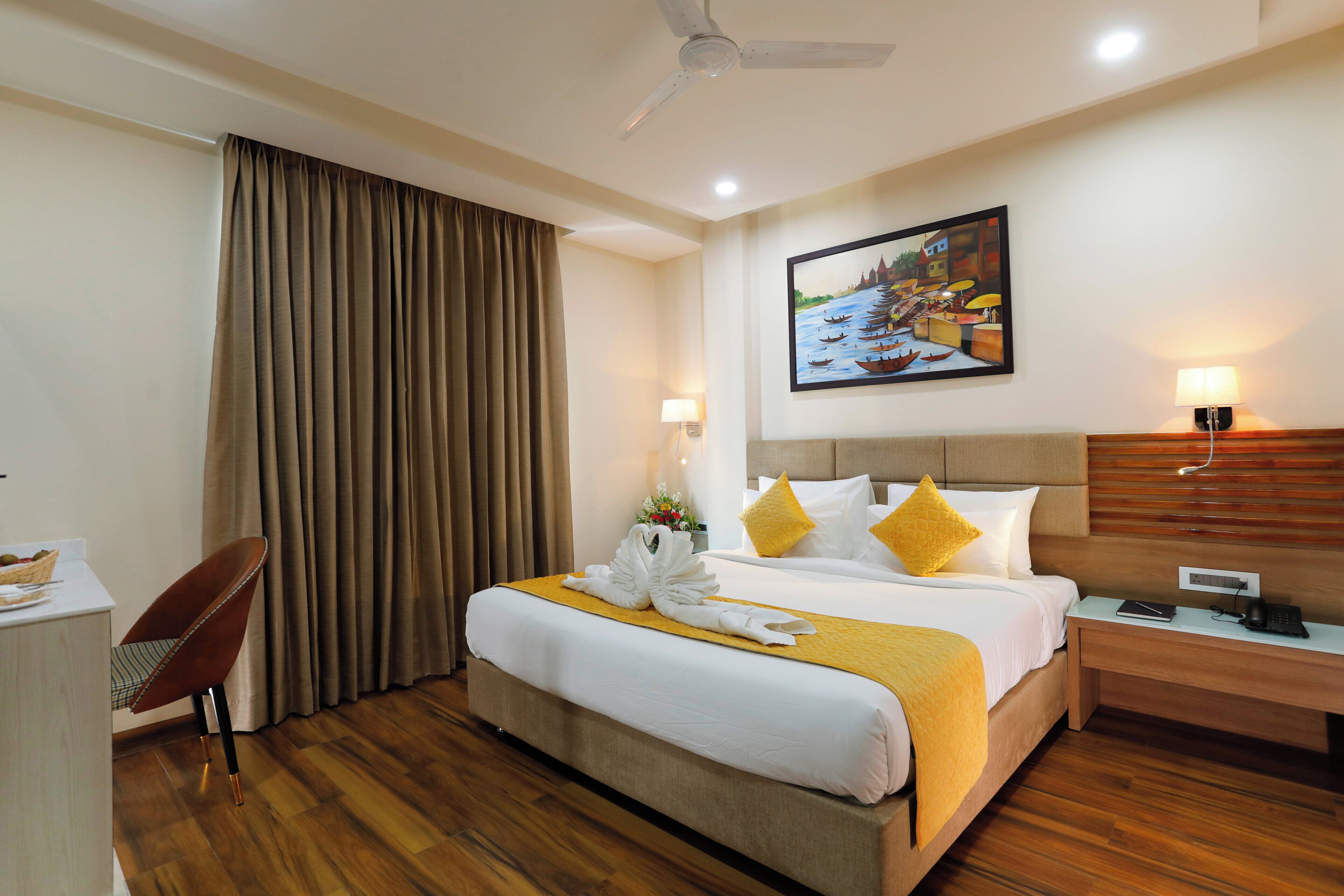 A hotel room with a bed, a desk, a chair, a nightstand, and a painting on the wall.