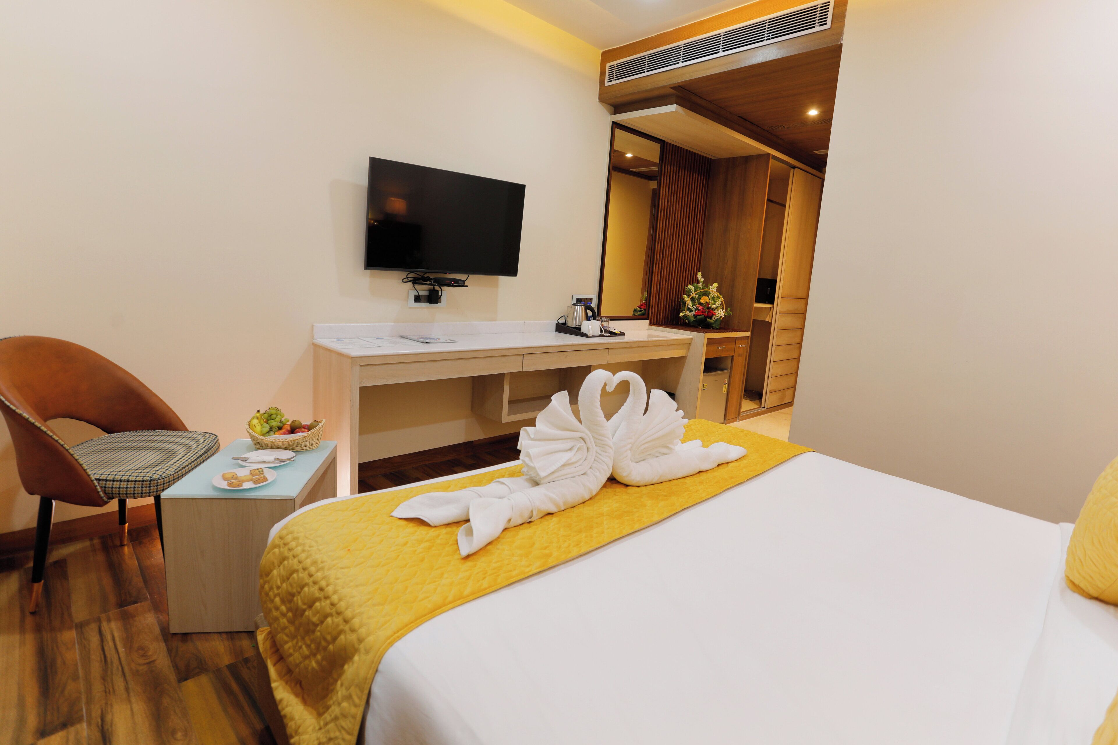 A hotel room with a bed, a desk with a flat-screen TV, a chair, and a small table with a fruit basket and a plate.