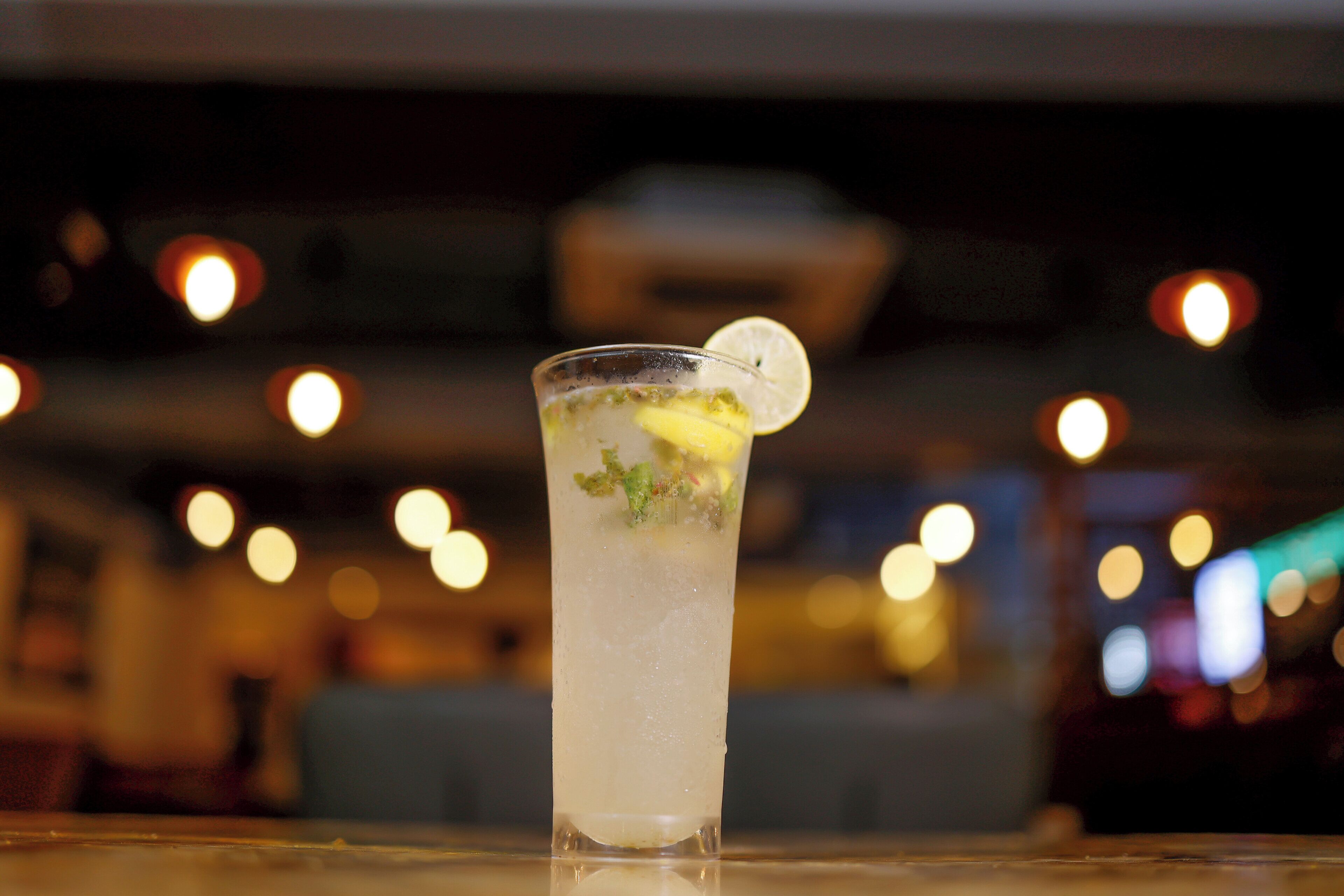 A clear glass with a lime wedge on a bar counter.