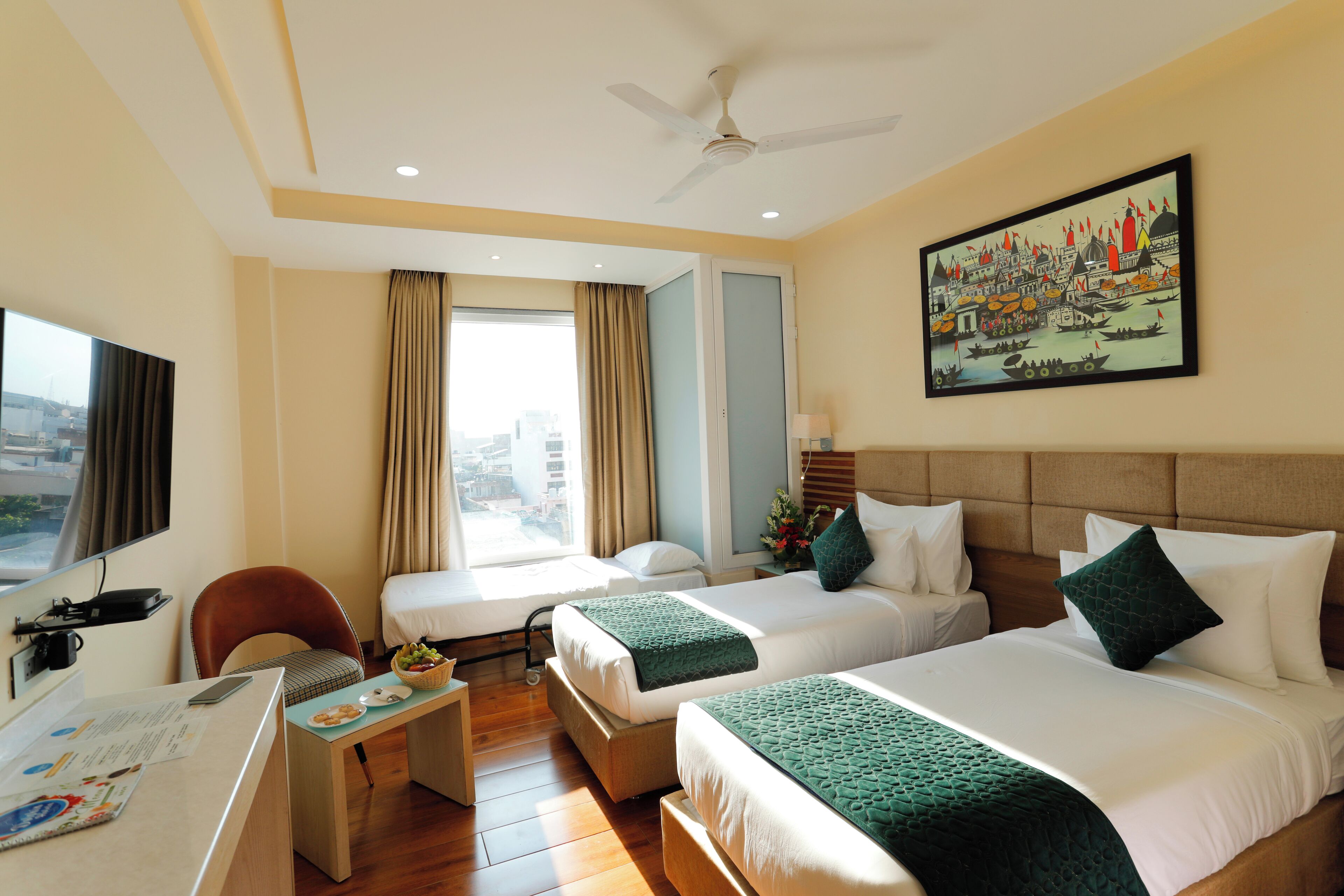 Habitación de hotel con dos camas, un escritorio, una silla, televisión y vista panorámica de la ciudad.