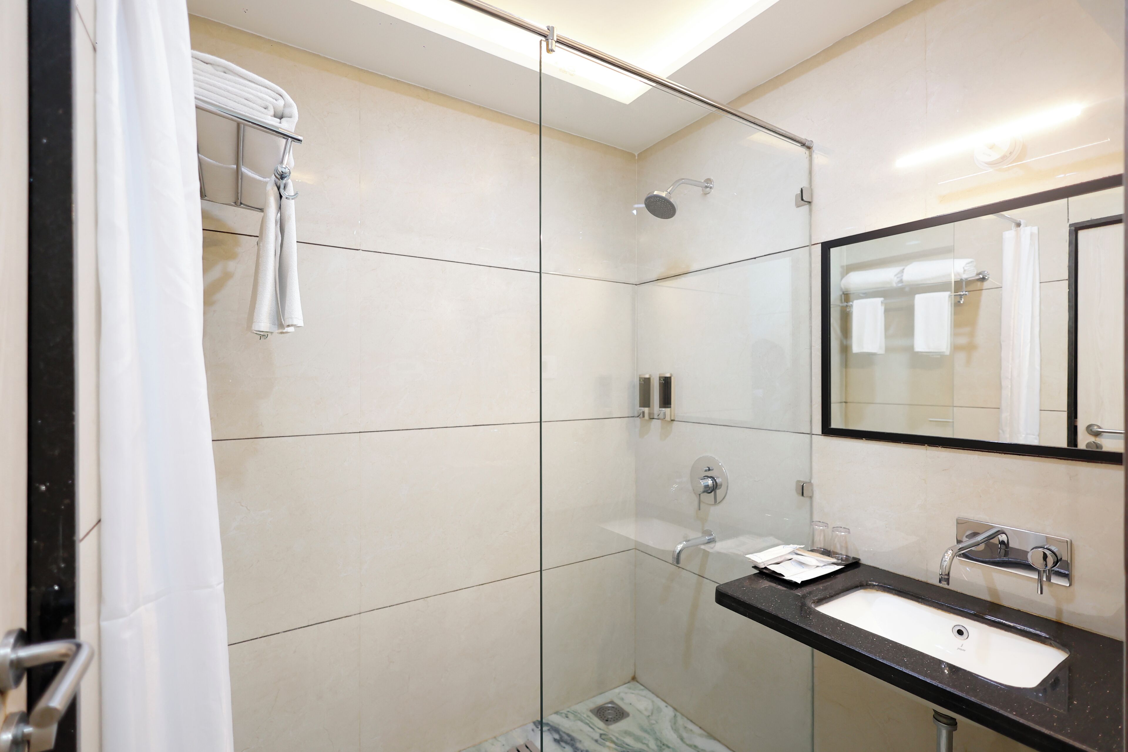 Un baño moderno con cabina de ducha de vidrio, lavamanos con encimera negra y un espejo grande.