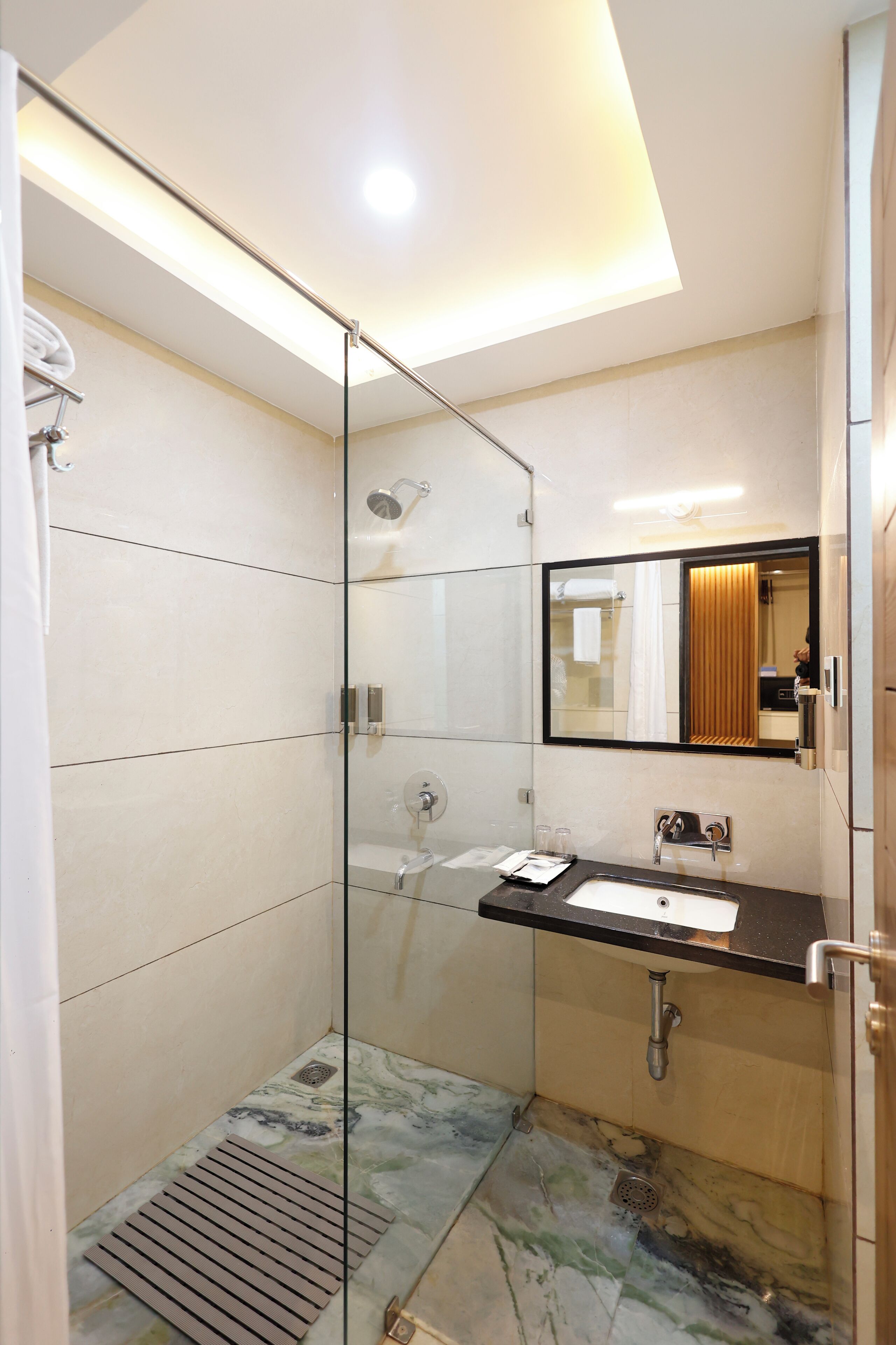 A modern bathroom with a glass shower enclosure, a marble-tiled floor, a black countertop with a sink, and a large mirror.