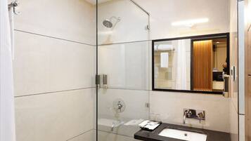 A modern bathroom with a glass shower enclosure, a marble-tiled floor, a black countertop with a sink, and a large mirror.
