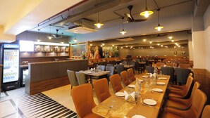 A restaurant with a long communal table, multiple dining booths, and a bar area. - HOTEL DOLPHIN GRAND  (Varanasi)