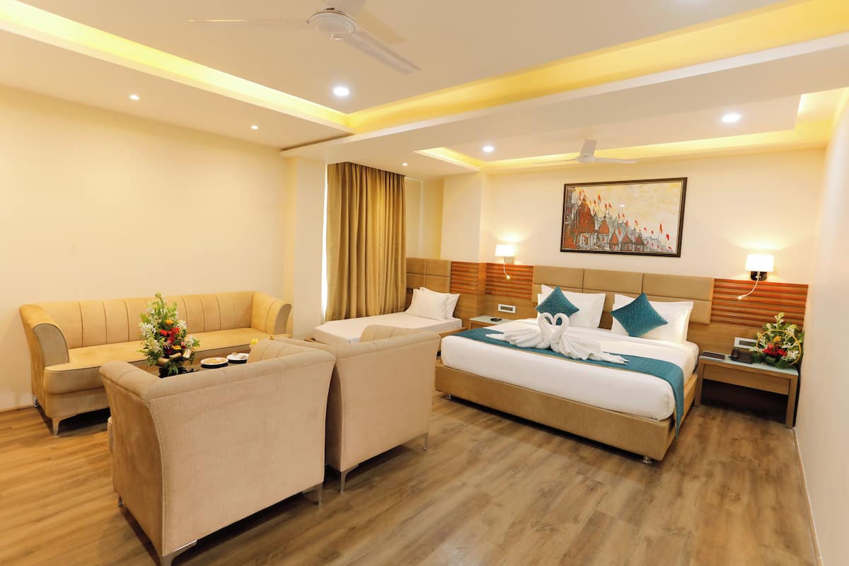 A hotel room with a bed, two armchairs, a sofa, a nightstand with a lamp, a painting on the wall, and a ceiling fan.