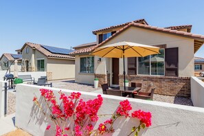 Ein Wohngebäude mit einer Terrassenfläche, ausgestattet mit Gartenmöbeln und einem großen Sonnenschirm.