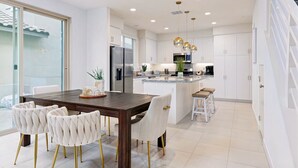 A modern kitchen with white cabinetry, a central island, and a dining area with a wooden table and upholstered chairs. - PGA West Luxury Villa/palm Springs:Golf,Pool,Fitness center (La Quinta)