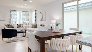 A modern living room with a dining area, featuring a large wooden table, white upholstered chairs, and a sofa set. - PGA West Luxury Villa/palm Springs:Golf,Pool,Fitness center (La Quinta)