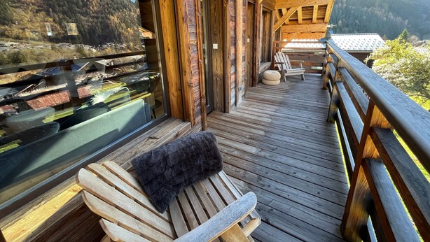 A wooden deck with a bench and a table, overlooking a mountainous landscape.
