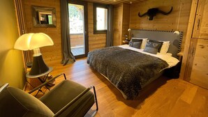A wooden cabin bedroom with a bed, a chair, a lamp, and a large window.