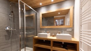 A modern bathroom with a glass-enclosed shower, wooden vanity with two sinks, and a large mirror.