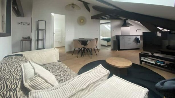 En modern lägenhet i loftstil med synliga takbjälkar, ett matområde, ett kök och ett stort fönster.
