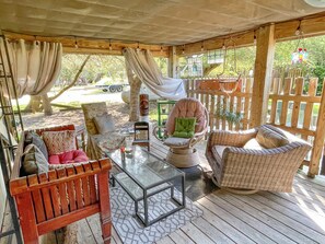 Relax in this serene outdoor seating area with a wicker chair, cushioned bench, and wooden bench, surrounded by lush greenery.