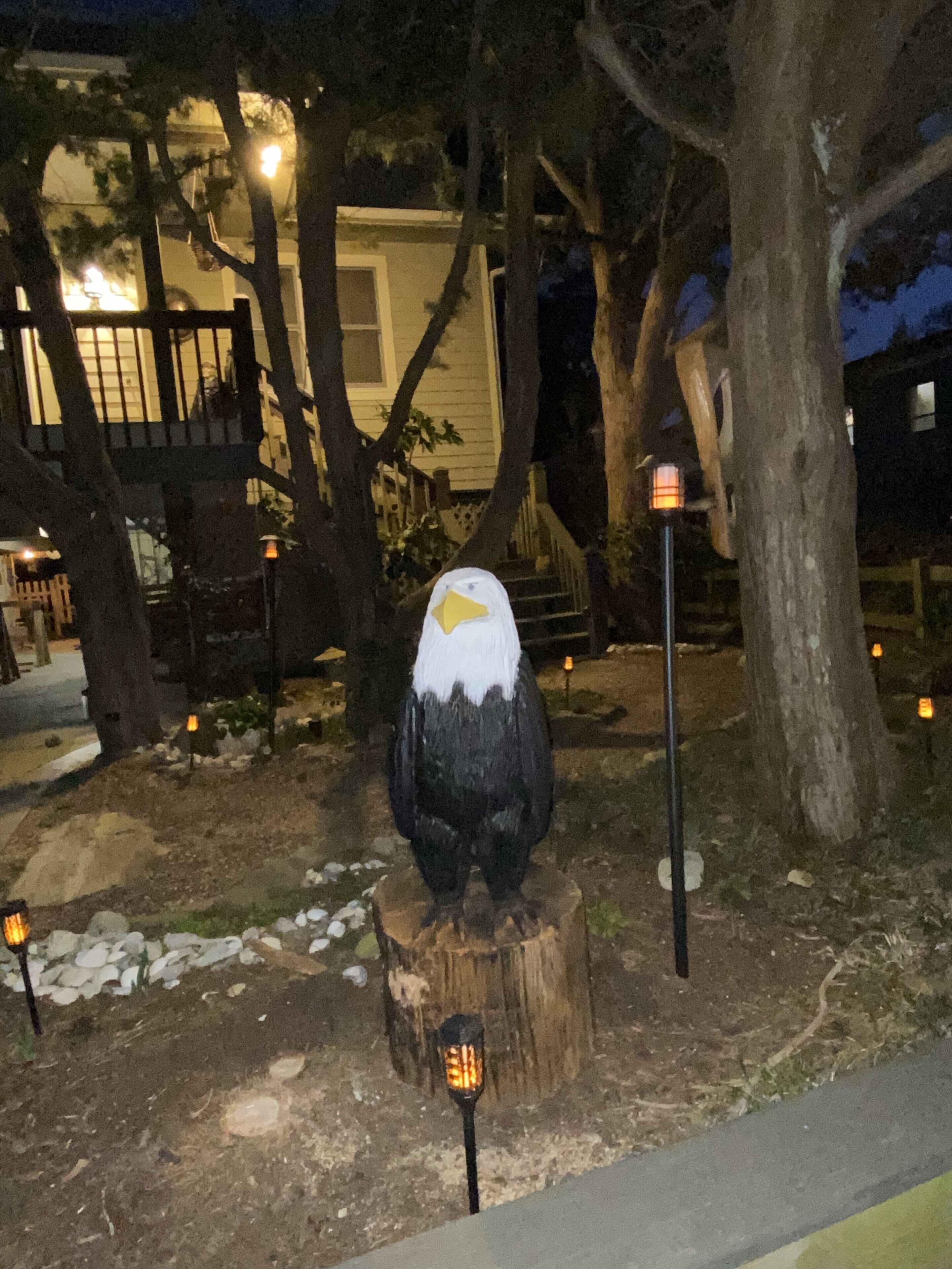 Eine große Vogel-Skulptur auf einem Baumstumpf, in der Nähe ein Laternenpfosten.