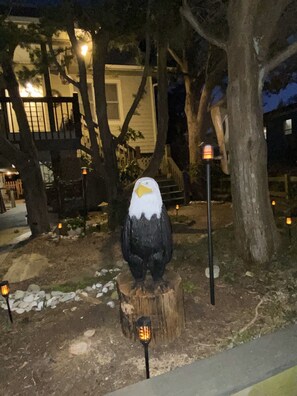 A large bird sculpture on a tree stump with a lamp post nearby.