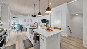 Una cocina moderna con una isla central, iluminación colgante y un comedor con sillas azules.