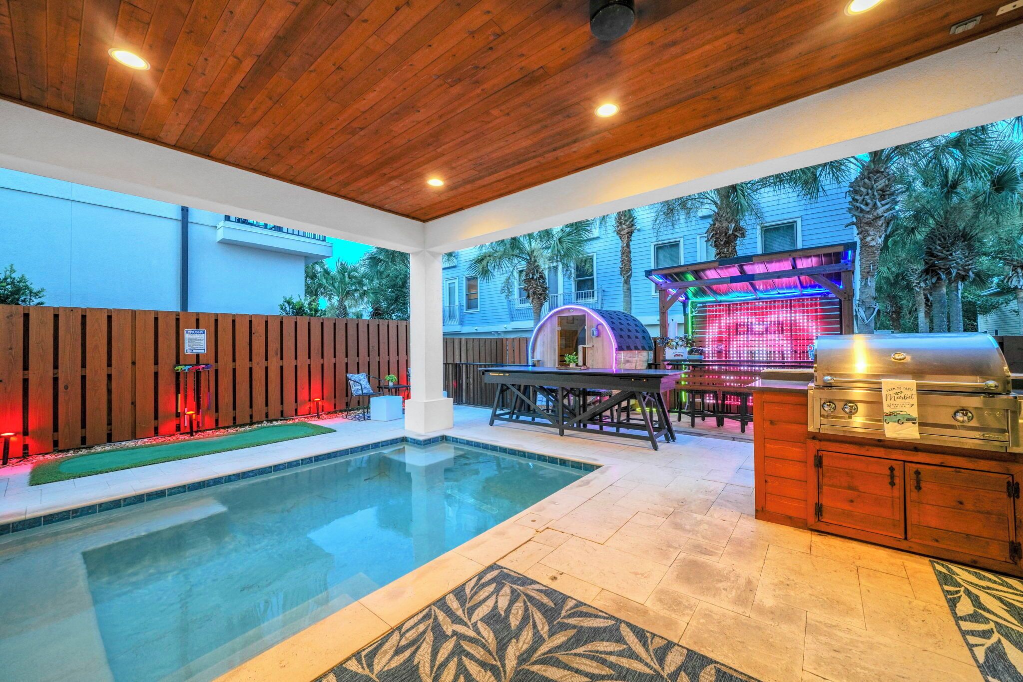 Un patio trasero con piscina, zona de barbacoa y terraza de madera.
