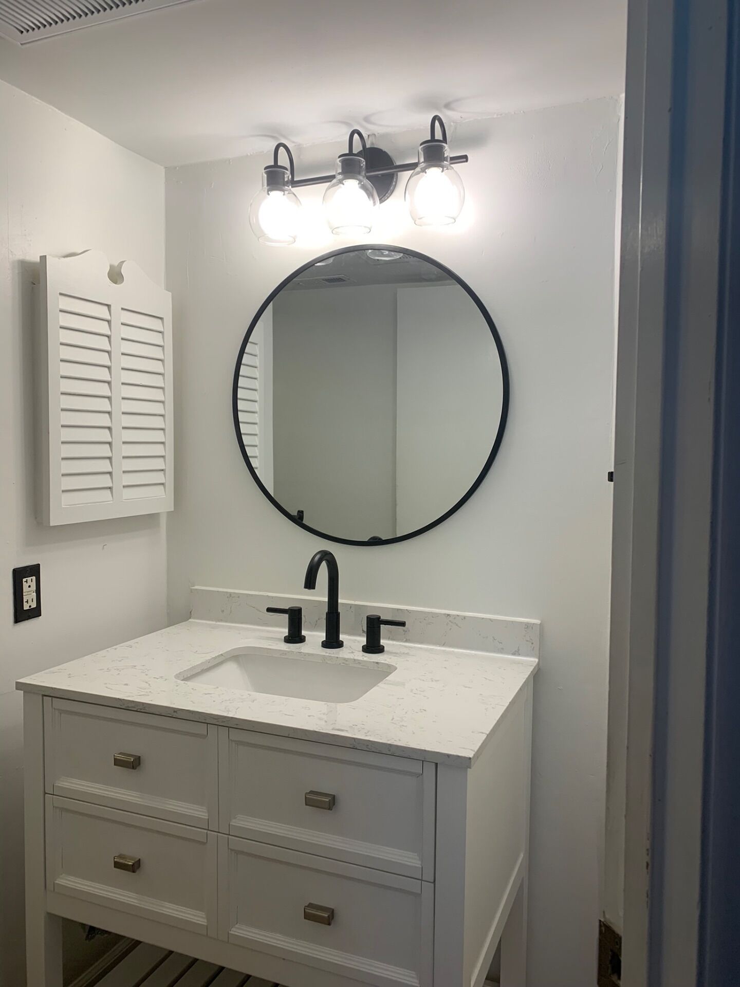 Une salle de bain avec un meuble-lavabo blanc, un miroir rond et trois luminaires placés au-dessus du miroir.