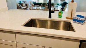 Een keuken met een RVS spoelbak, een fles afwasmiddel en een stap opgevouwen handdoeken op het aanrecht.
