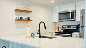 Een moderne keuken met een groot eiland, barstoelen, een magnetron en een koelkast.
