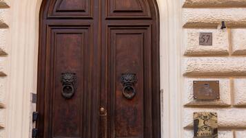 Puerta doble de madera con aldabillas metálicas ornamentales, una placa con el número '57' y un letrero que indica 'CAVOUR LUXURY ROOMS'.
