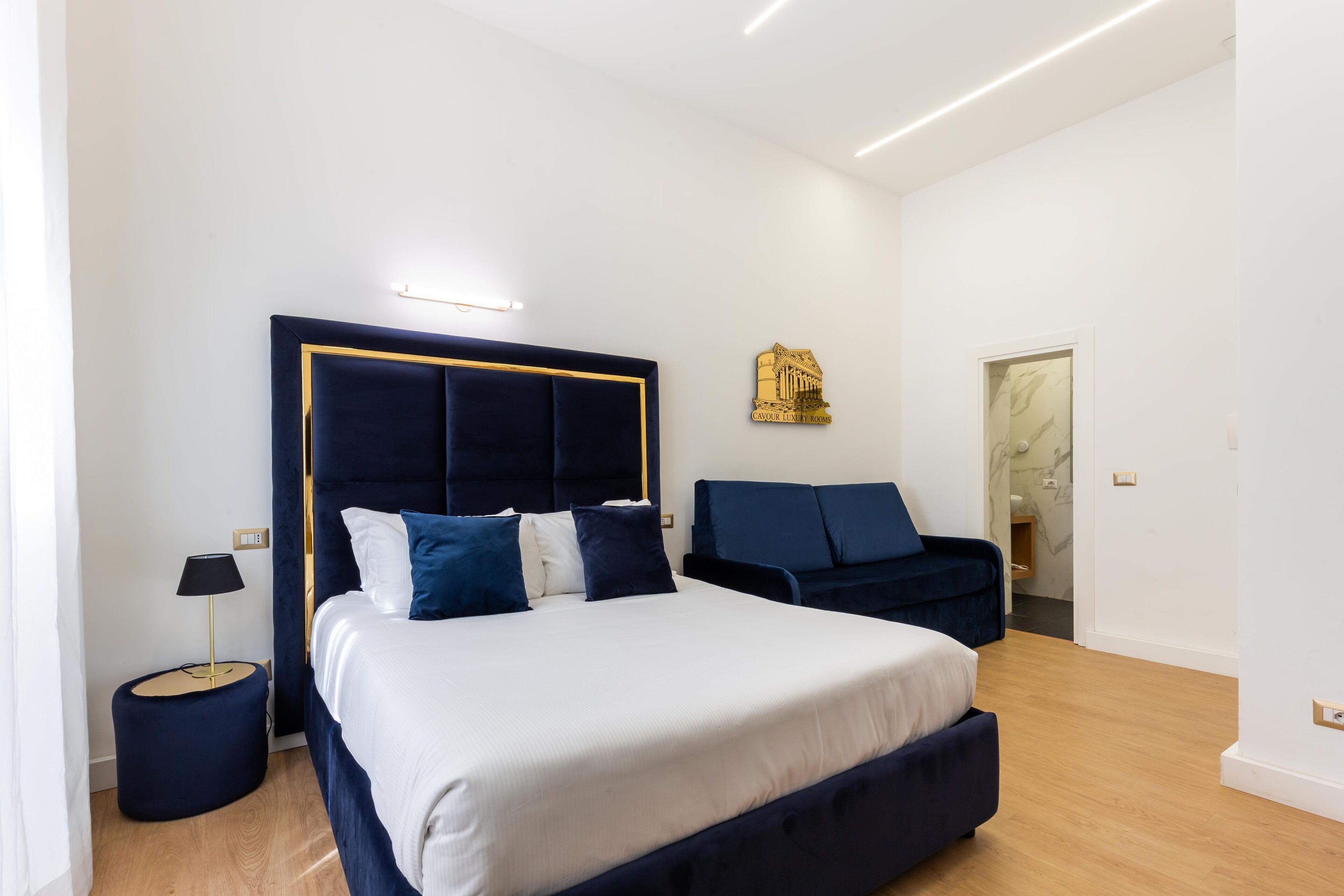 A modern bedroom with a large bed, a bedside table, a chair, and a wall-mounted light fixture.
