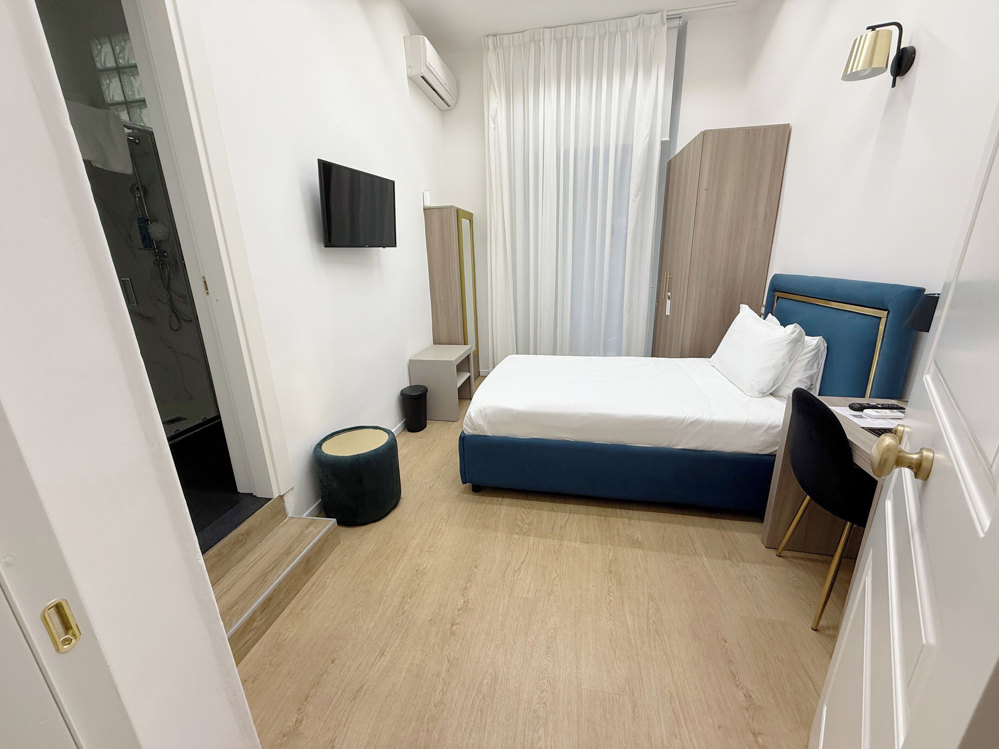A modern hotel room with a bed, a desk, a chair, a TV, and a bathroom with a shower and toilet.