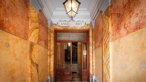 Un pasillo de mármol con suelo a cuadros, un cartel que dice “Anno 1887” y una puerta de madera al final.