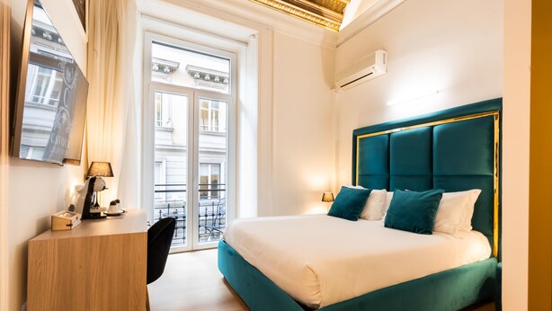 Habitación de hotel moderna con una cama grande, un escritorio y vistas a la calle a través de un ventanal.
