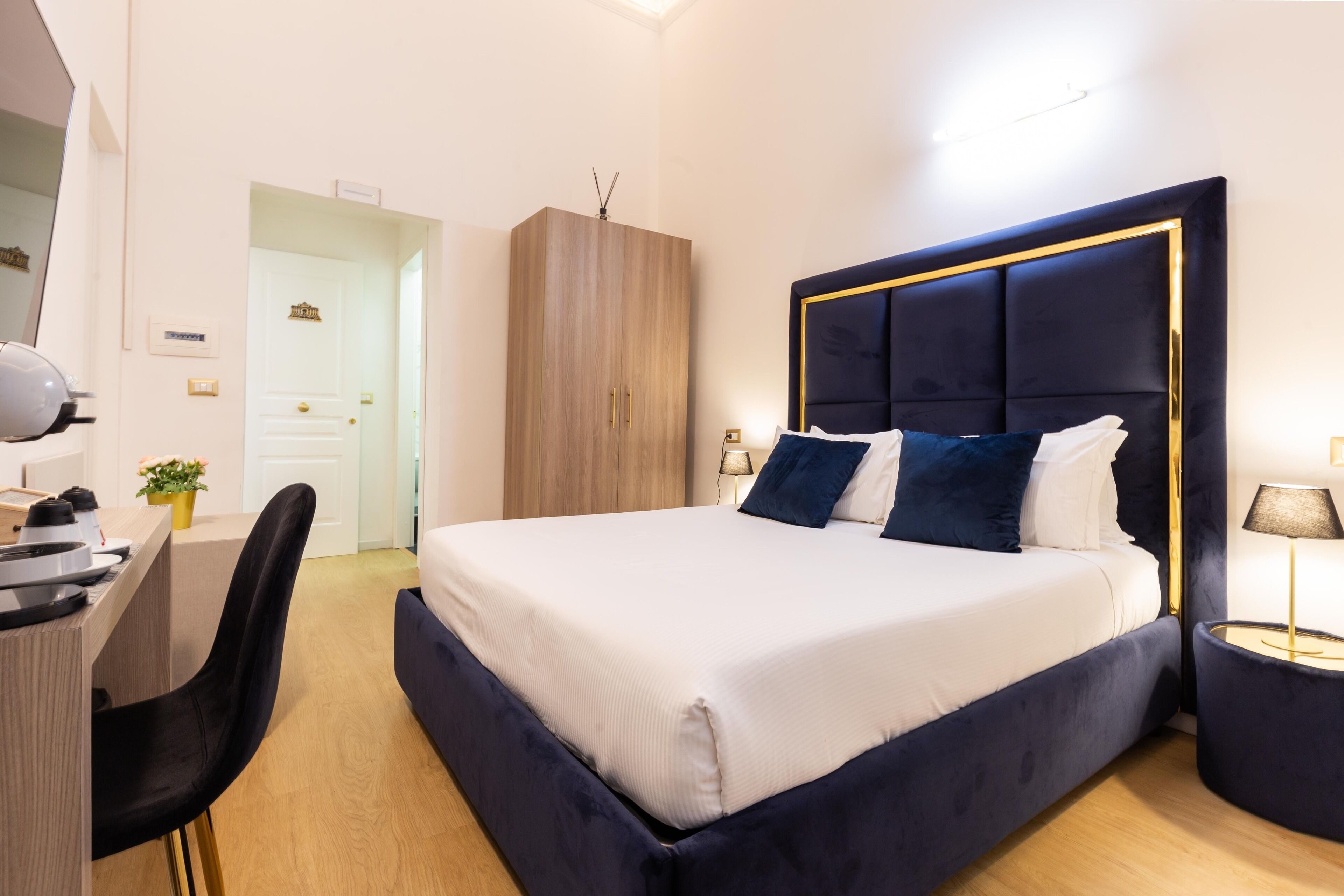 A modern hotel room with a large bed, a desk, and a wardrobe.