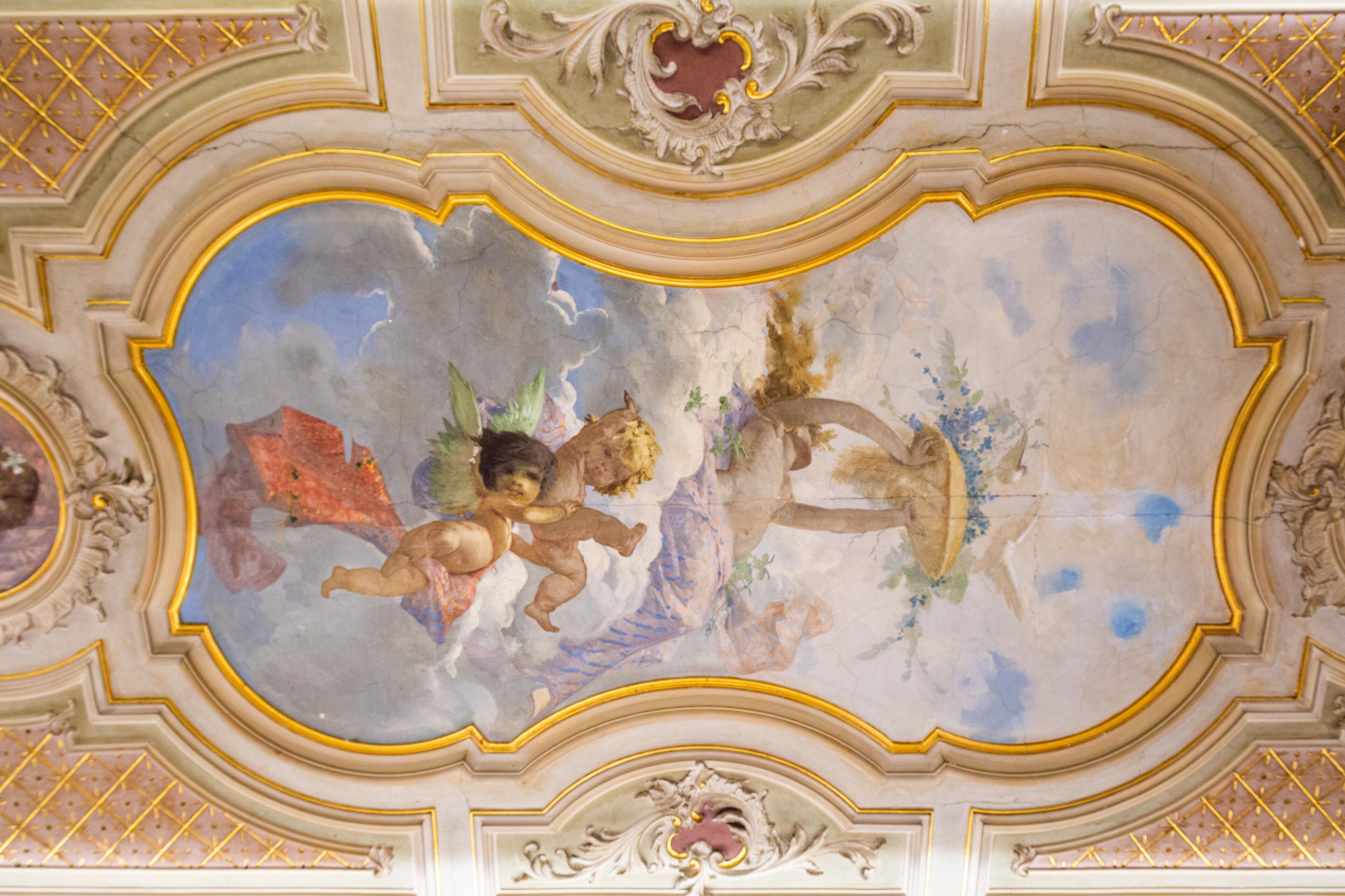 A ceiling with ornate gold detailing and a fresco of cherubs.