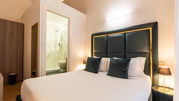 Habitación de hotel con una cama grande, una mesita de noche con lámpara, un armario de madera y un baño visible a través de una puerta abierta.