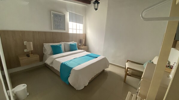 Une chambre à coucher comprenant un lit, des tables de chevet, une commode, une fenêtre, une lampe fixée au mur et une chaise.