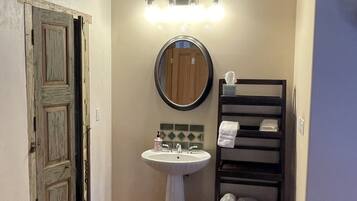 A bathroom with a wooden door, a pedestal sink, a mirror, and a towel rack with towels.