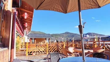 An outdoor patio with tables and chairs, a wooden deck, and a view of mountains in the background.