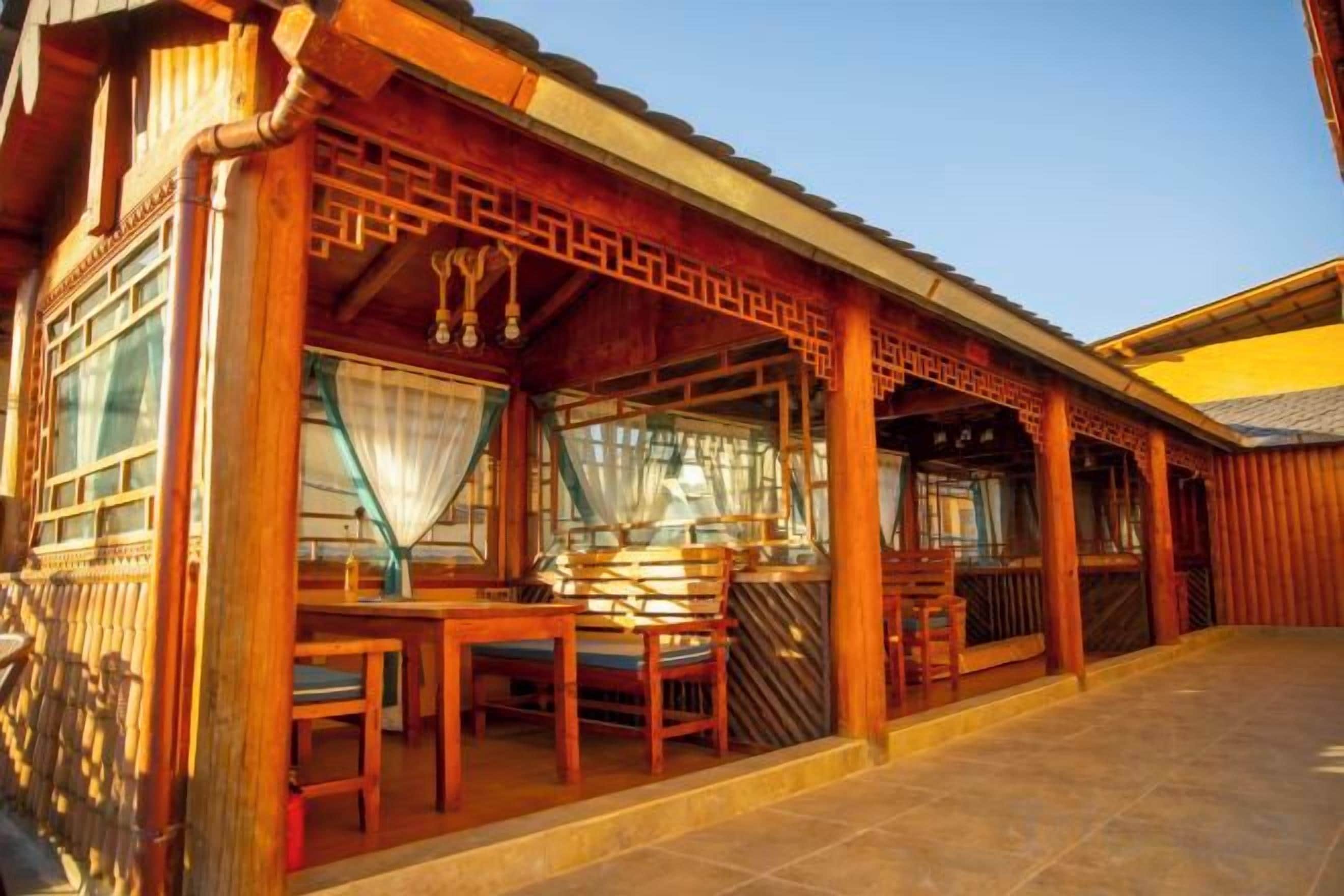 A traditional wooden building with a covered porch, a table with chairs, and a window with curtains.