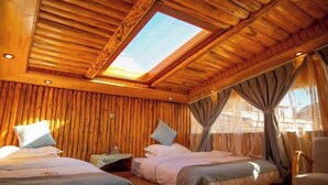 A wooden cabin room with a skylight, two beds, a chair, and a small table. - Spring Breeze Inn (Shangri-La)