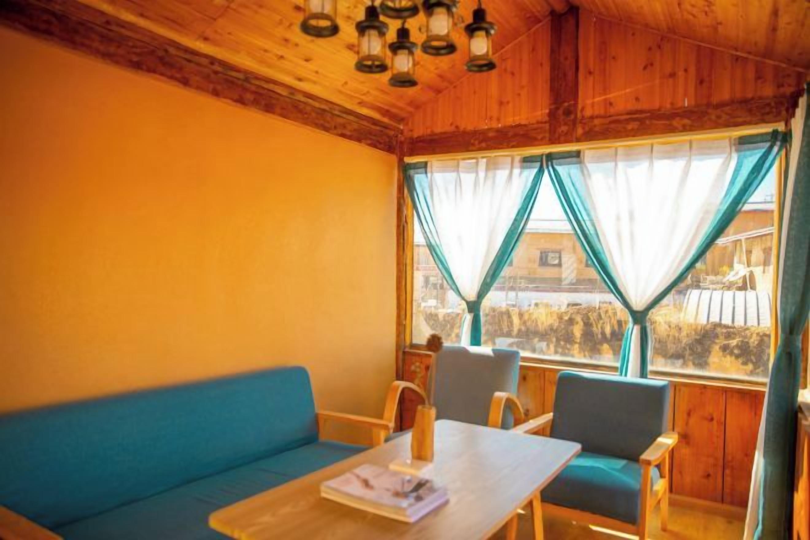 A room with a wooden ceiling, a blue sofa, a wooden table with a candle, and two chairs.